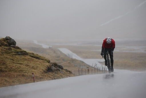 Cyklist trampar uppför en våt väg i kraftigt regn