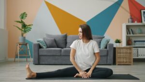 Kvinna gör en sittande höftstretch på en yogamatta i vardagsrummet
