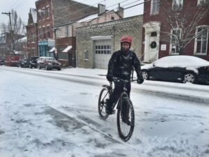 Cyklist trampar genom snöfall på en vintertäckt stadsgata